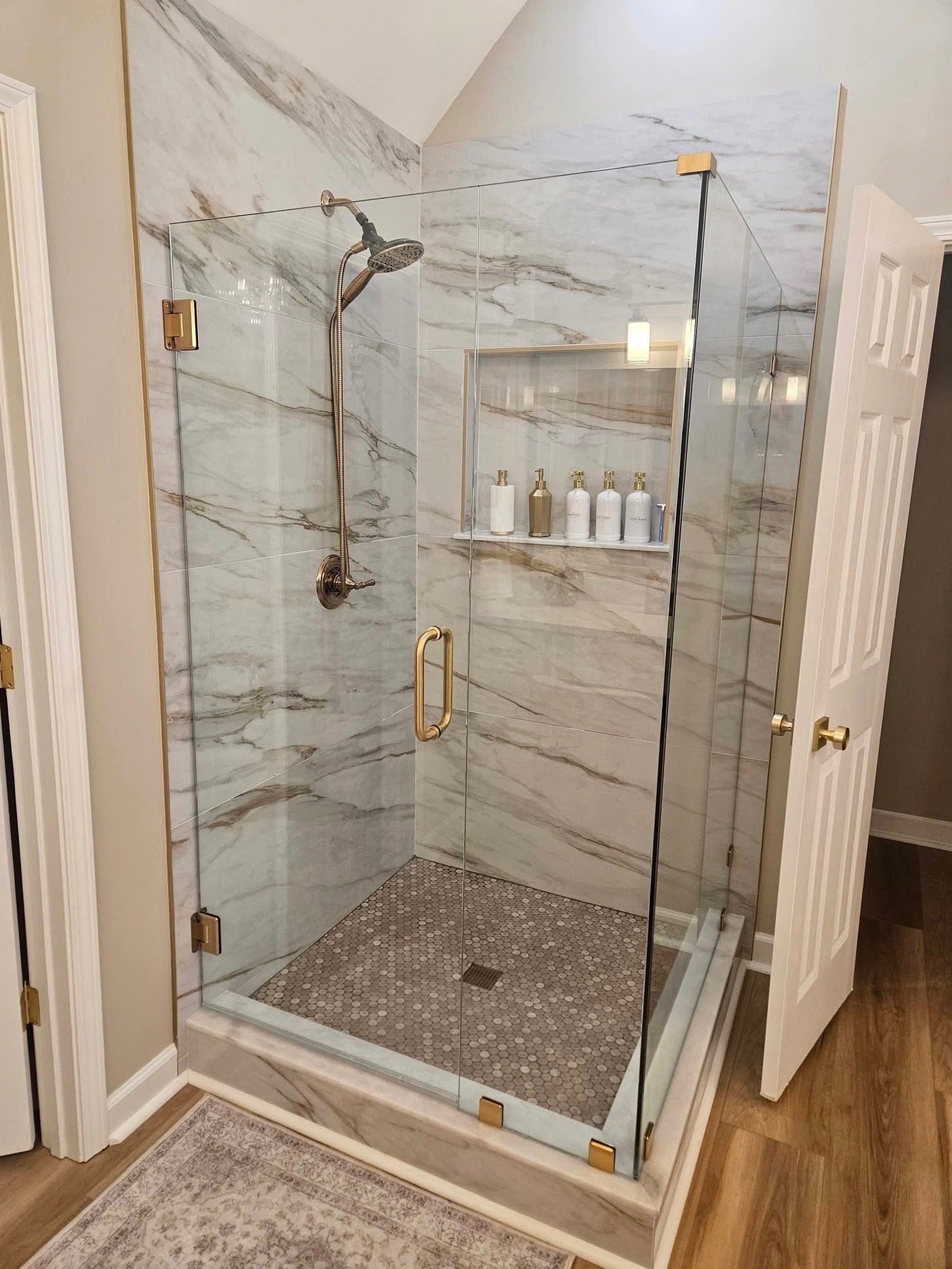 Frameless glass shower with marble tile and gold fixtures by Talbot's Remodeling